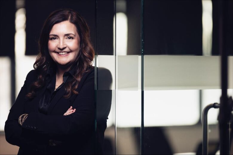 A woman with long brown hair smiles as she leans in the doorway of a conference room.