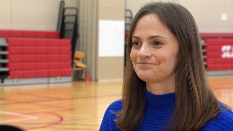 A smiling woman with long brown hair stands in a gymnasium.