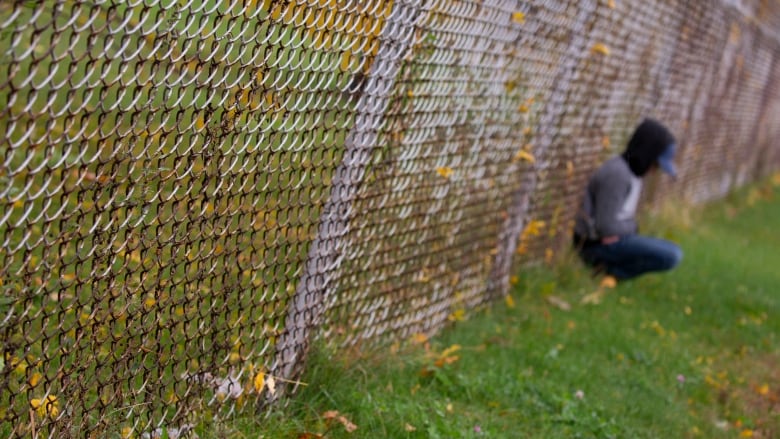 A boy sits alone against a fence. 