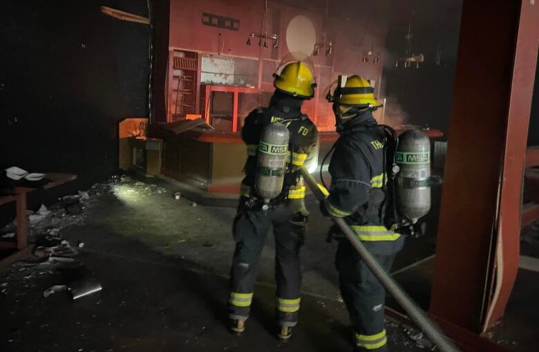 Two firefighters carry a hose into a room.