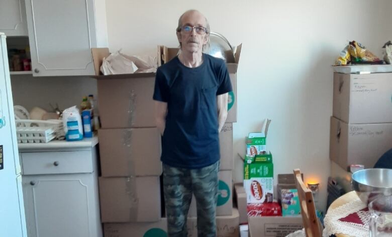 A man wearing a blue t-shirt and camouflage pants stands posing for a photo in an apartment suite.