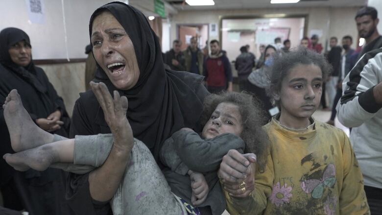 An adult reacts while carrying a child covered in dust and holding the hand of another at a hospital