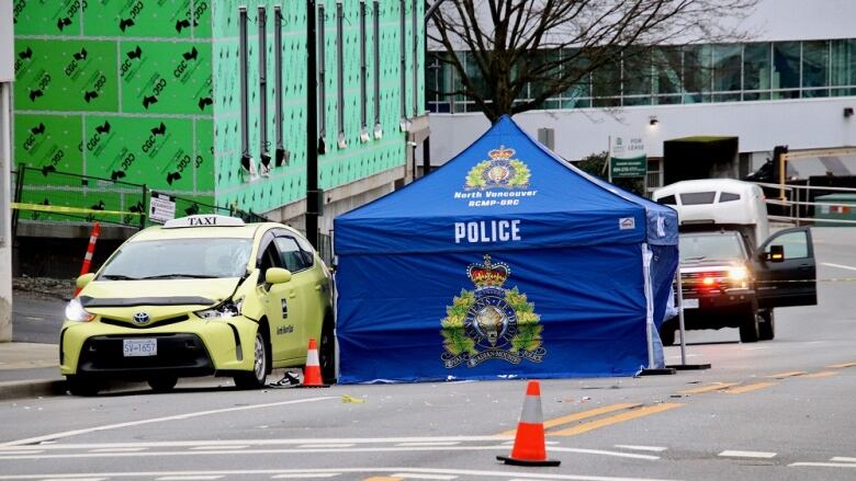 A yellow taxi with a dent in the front is pictured beside an RCMP police tent on the street. 