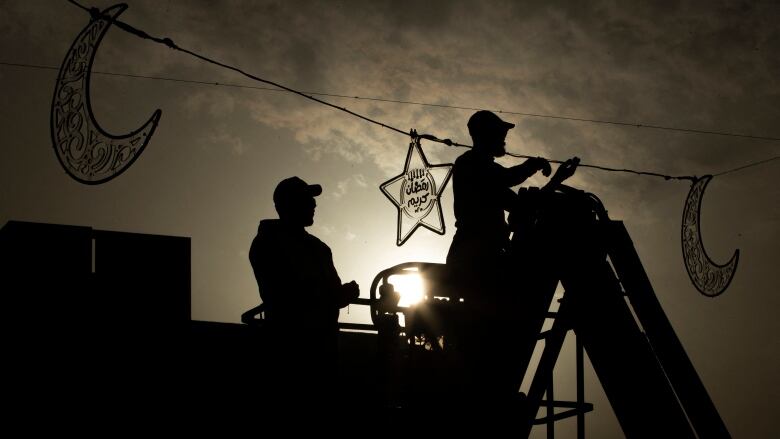 Workers install crescent and star-shaped decorations on a line. 