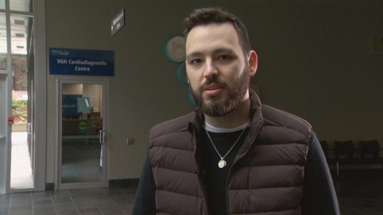 A young university student stands near Vancouver General Hospital with a cardiology sign in the background.