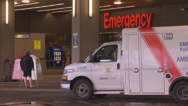 A patient with crutches stands near an ambulance outside a hospital Emergency Department.