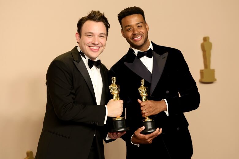 Two men pose with Oscar awards.