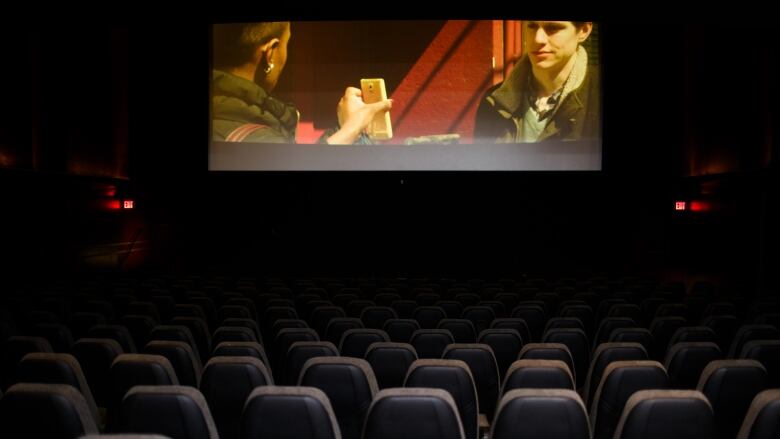 Photo showing an empty cinema screening room with a film playing. 