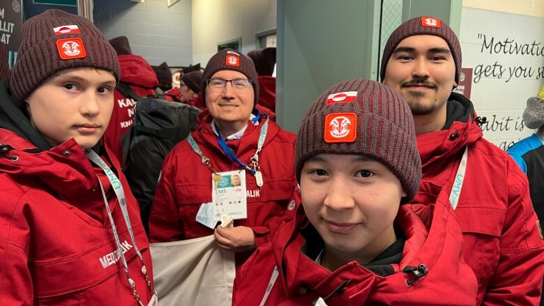 Four people wearing red jackets and hats look at the camera 