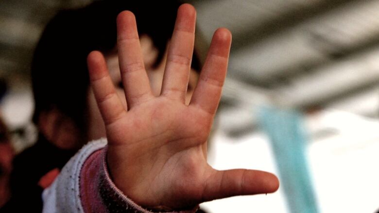 A child's hand is held up to the camera, blocking their face. 