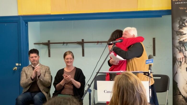 Two people embrace behind a podium. 