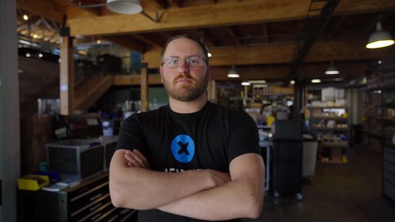 A man in glasses and a short-sleeved black t-shirt poses with his arms crossed.