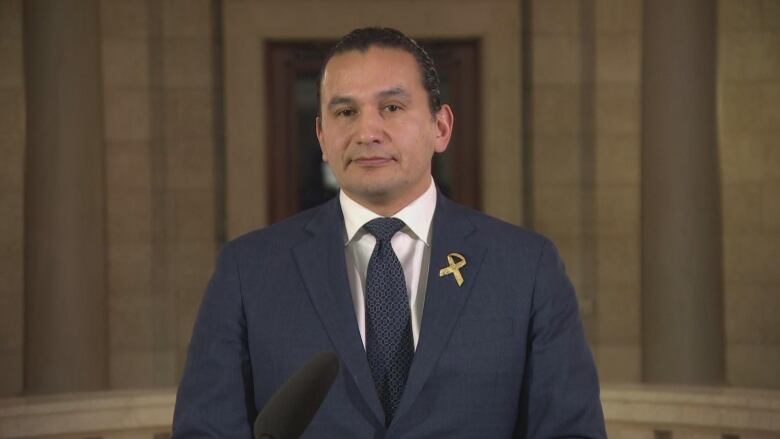 A man in a navy blue suit and tie is pictured looking forward.