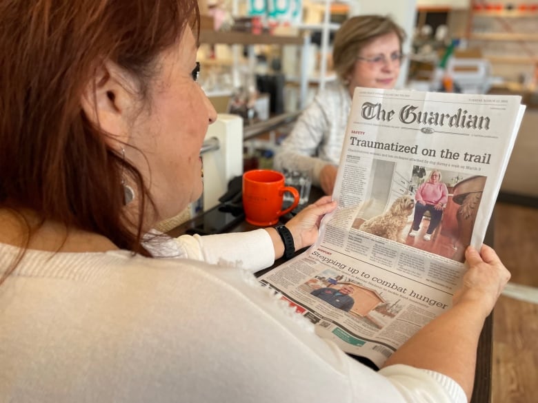 A woman reads the front page of a newspaper.