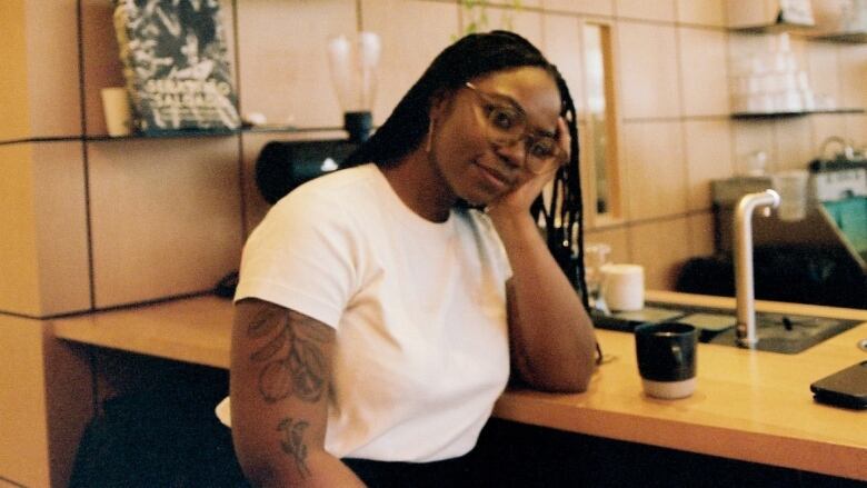 Woman sitting at a bar wearing a white t-shirt and glasses. 