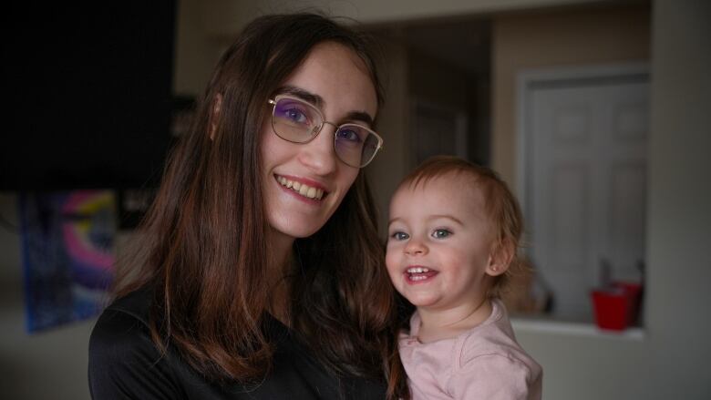 A woman with glasses and auburn hair holds a baby.