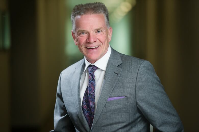 A man in a grey suit smiles at the camera.