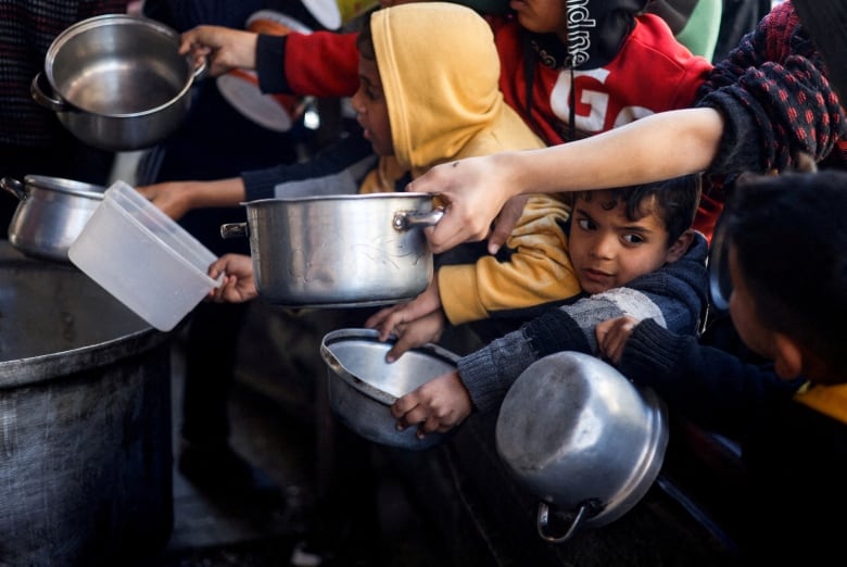 Children hold out silver bowls waiting for food from a charity kitchen.