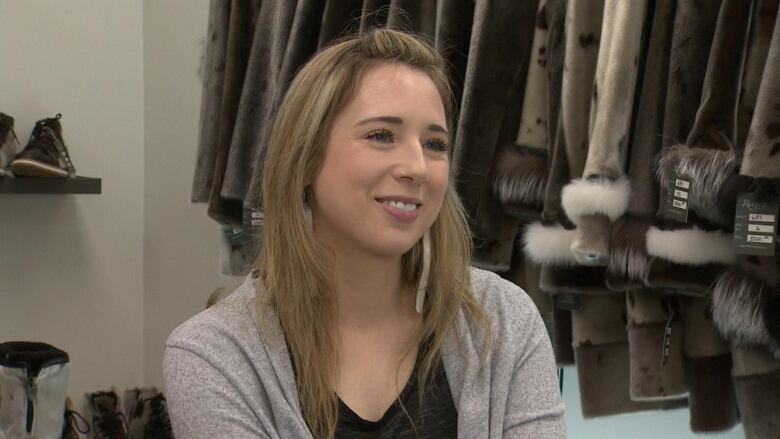 A woman sits in a store with seal boots and coats in the background. 