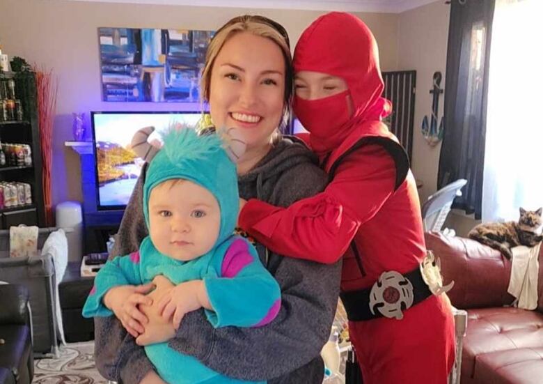 A woman holds two young children in Halloween costumes