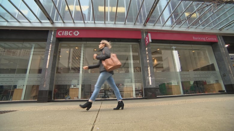 A blurry silouette of a woman walking by a CIBC location.