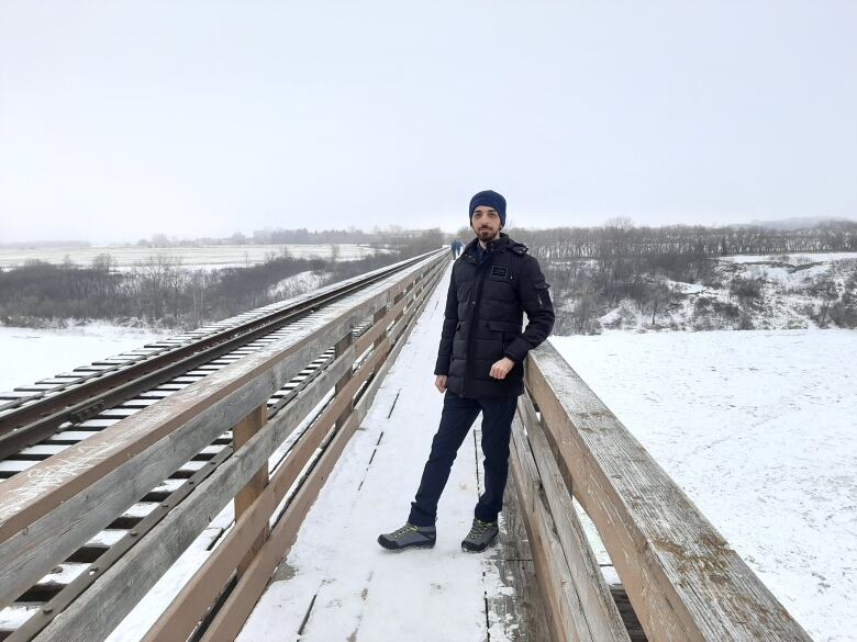 A man in a parka along snowy railway tracks.