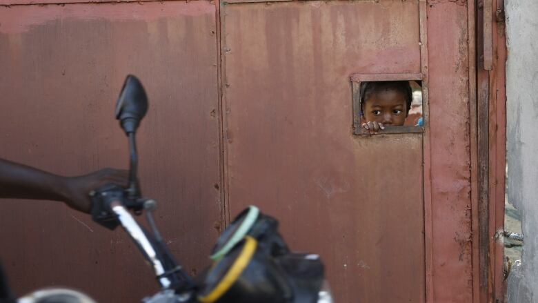 A child watches from an opening in a security gate as residents flee their homes due to gang violence in Port-au-Prince, Haiti on Saturday, March 9, 2024.