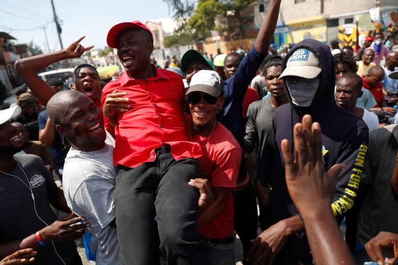 Opposition politician Jean-Charles Mose of the Pitit Desalin party is lifted by supporters who came to greet him from the roadside, as he leads several hundred protesters through the Tabarre neighborhood toward the United States embassy, in Port-au-Prince, Haiti, Thursday, Oct. 17, 2019. Protesters marched to the embassy to demand that the U.S. stay out of Haiti's politics. (AP Photo/)