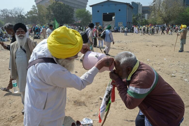 A farmer gives drinking water to another during a protest.