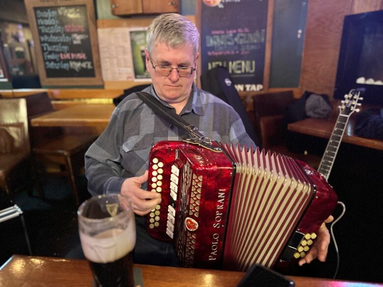 a man in a grey shirt plays a red accordion inside a pub