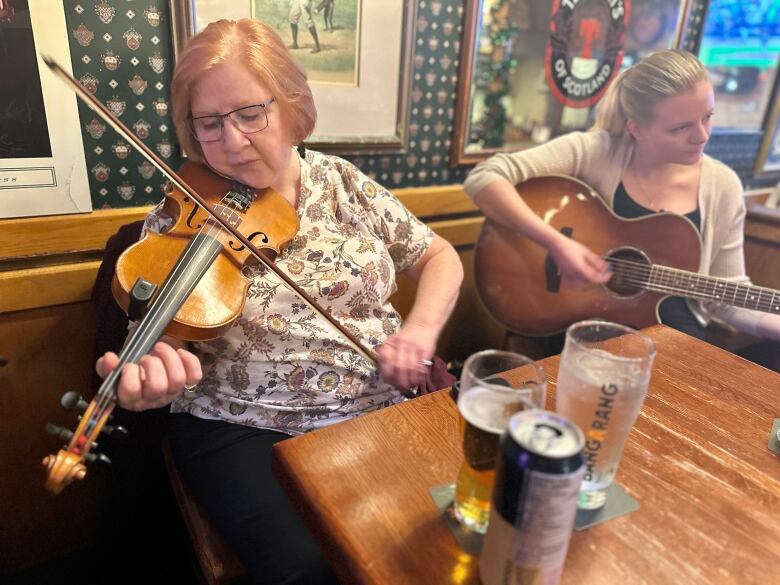 one woman plays fiddle while the other plays guitar