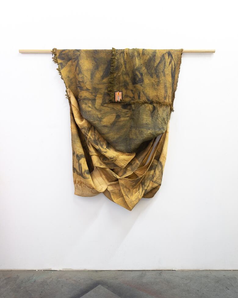 A wall hanging of muddy draped yellow fabric.