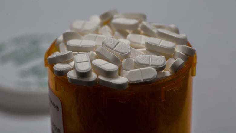 An orange prescription drug bottle nearly overflowing with pills is shown in close-up.