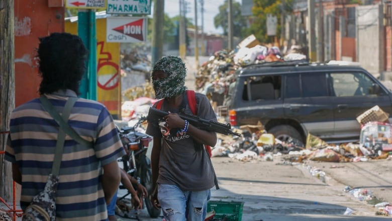 Masked men with guns stand next to a street filled with trash and debris.