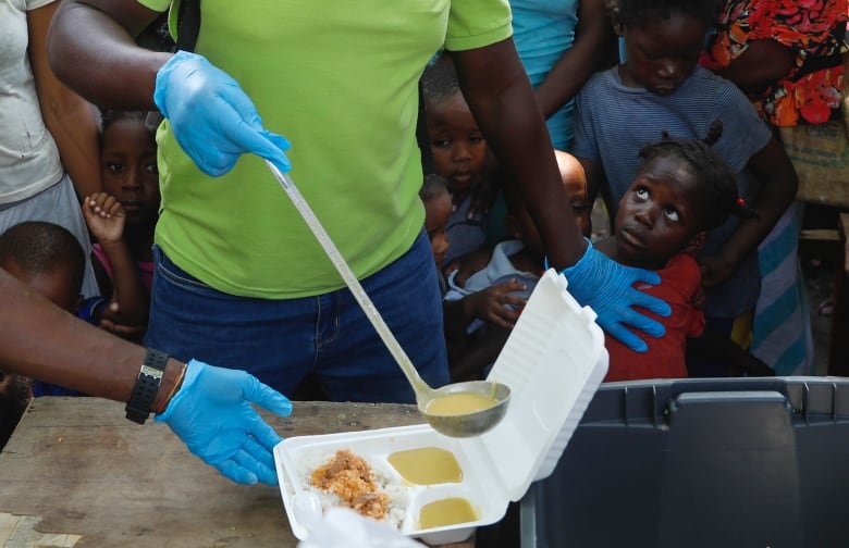 A server ladles soup into a container as children line up to receive food at a shelter for families displaced by gang violence in Port-au-Prince, Haiti on Thursday, March 14, 2024.