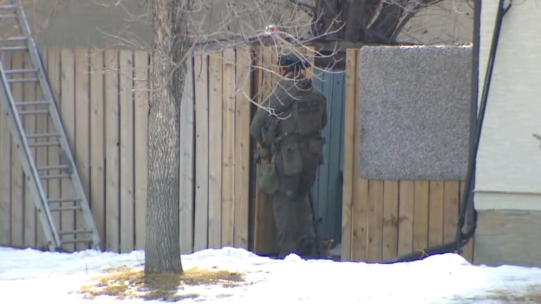 A Calgary police officer guards a gate on a fence line near the standoff.