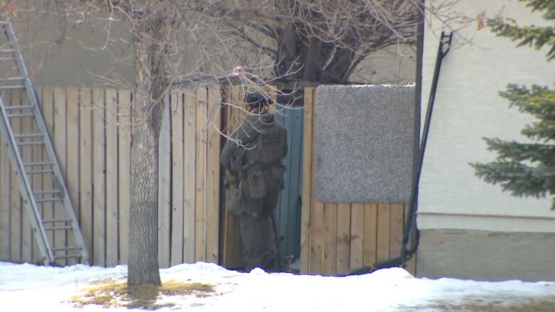 A Calgary police officer guards a gate on a fence line near the standoff.