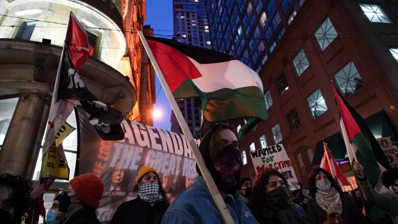 Protesters gather outside with Palestinian flag.