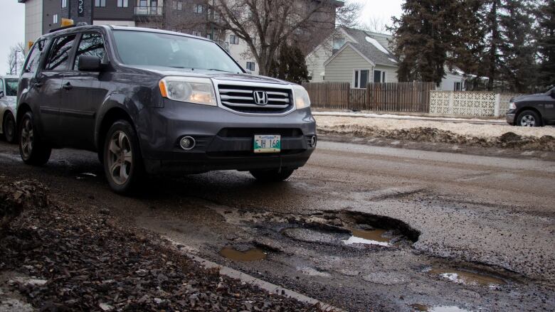 A car drives by a big pothole.