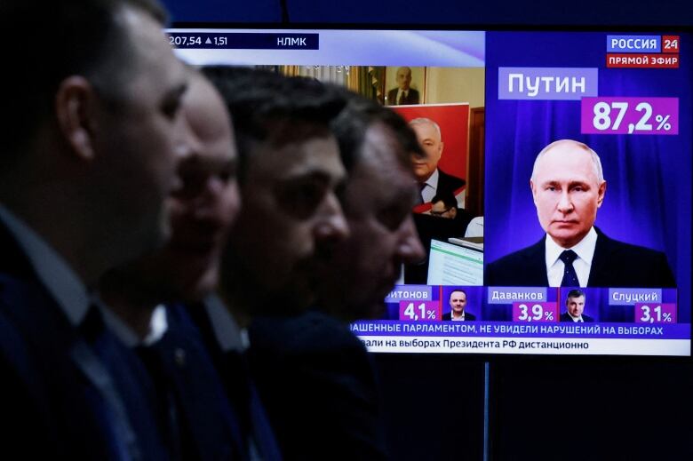 People sit in the foreground as a TV showing election results is seen behind them.