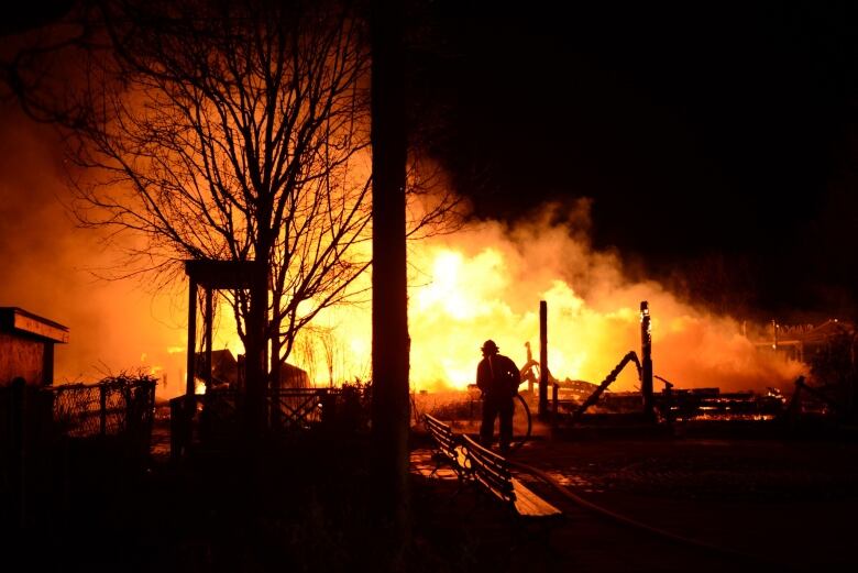 A fire eats away at a building. A firefighter is seen holding a hose.