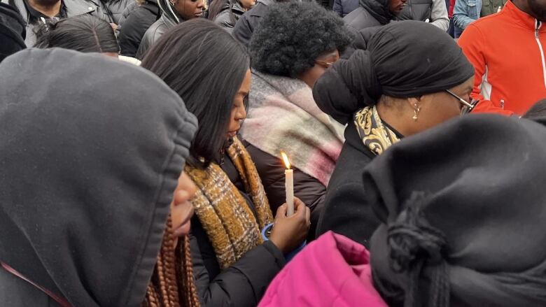 People are seen at a vigil. One woman holds a candle with her head slightly bowed.