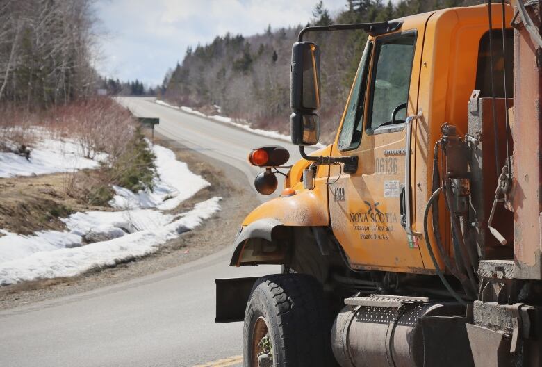 A large yellow highway truck is in the foreground, blocking a road leading uphill.