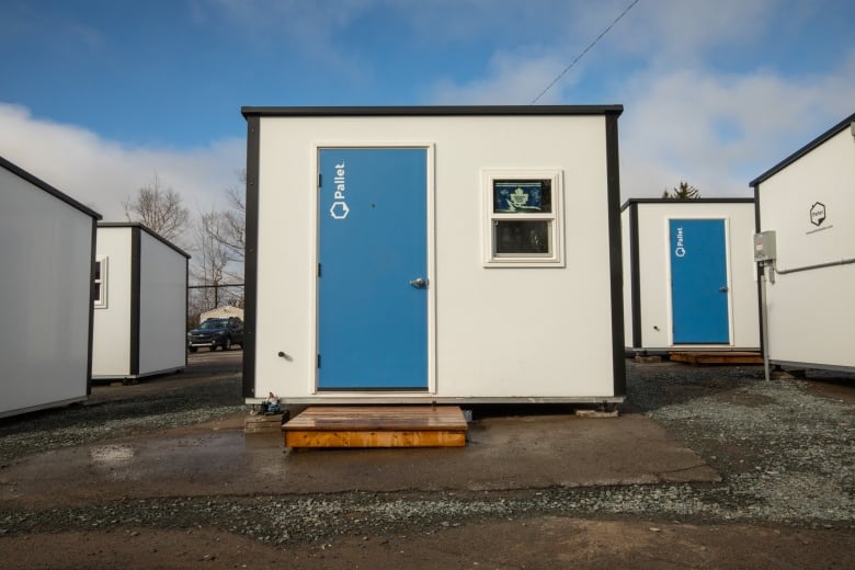 A closeup of the front of a small hut-like structure with white walls, a blue roof and a single window next to a blue front door.