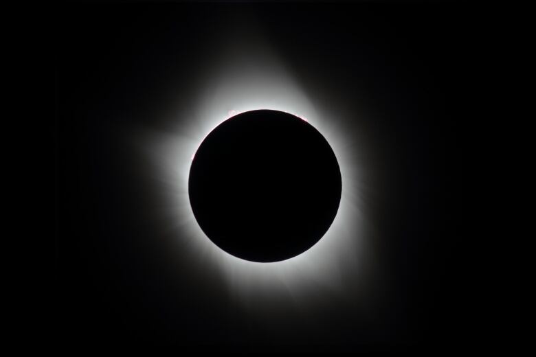 The sky appears black and a white ring is seen around the moon as it blocks out the sun during a total solar eclipse. 