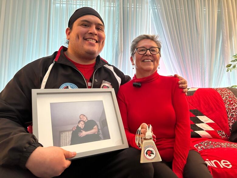 Josh Redbear Amos holds a picture of his late brother who was on the team while Darlene Amos hold a cowbell like the one her late mother use to always use. 