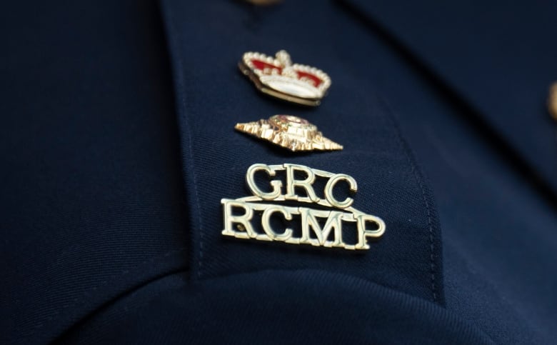 Closeup of a police logo that says GRC RCMP in gold lettering topped with a crown and a pin on a navy blue epaulette.