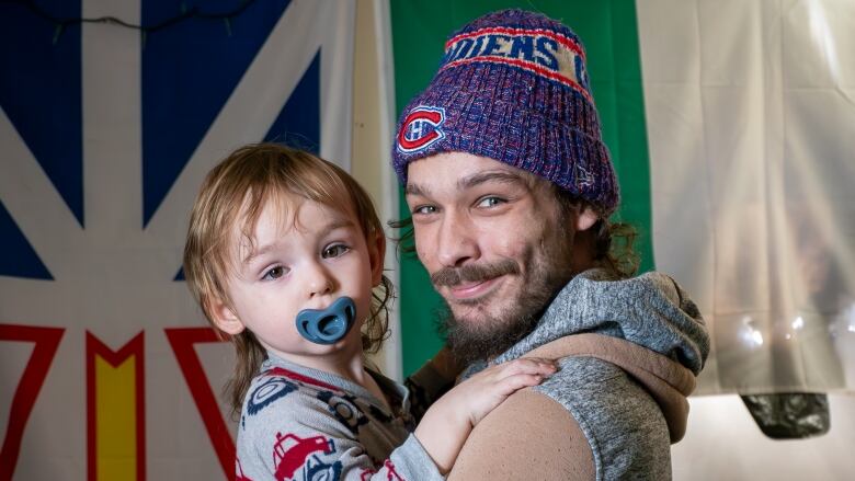 A person wearing a toque holds a young child who has a pacifier in their mouth.