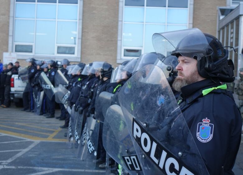 Police holding shields standing in a line.