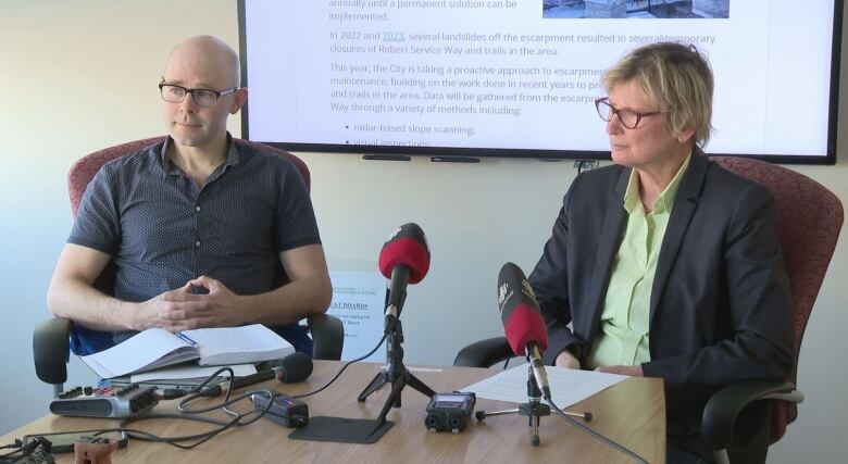 Two people sit at a table with microphones.